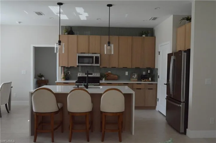 Kitchen with an island with sink, hanging light fixtures, stainless steel appliances, sink, and decorative backsplash