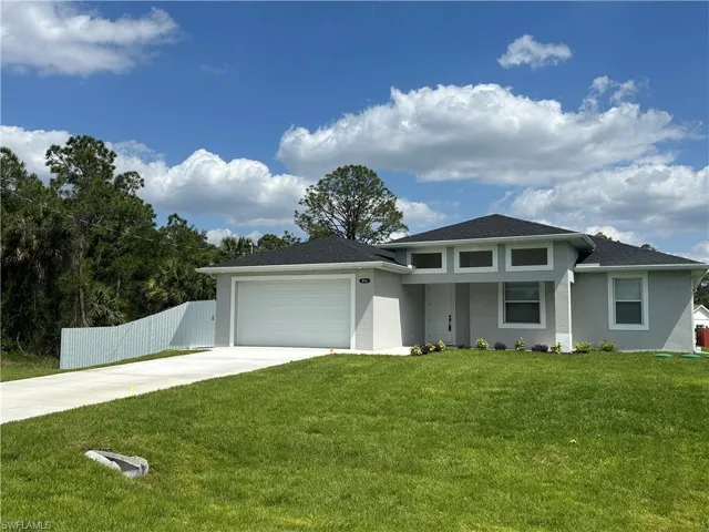 Prairie-style home with concrete driveway, a front lawn, an attached garage, fence, and stucco siding