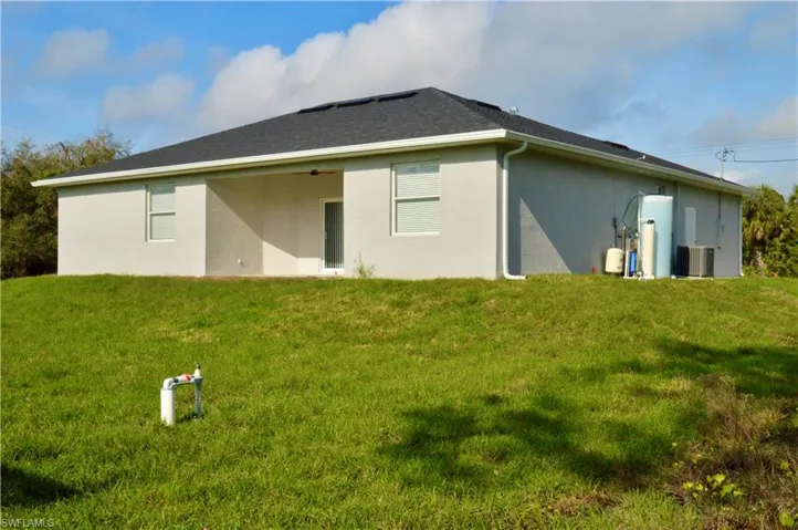 Rear view of property featuring a lawn and central AC