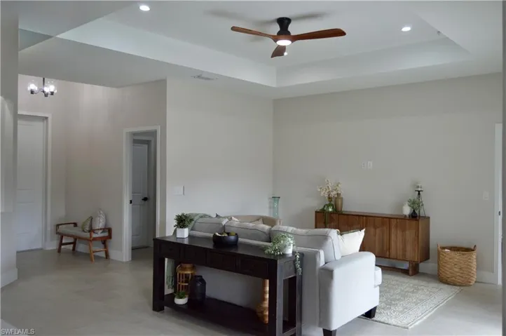 Living room featuring ceiling fan with notable chandelier and a tray ceiling