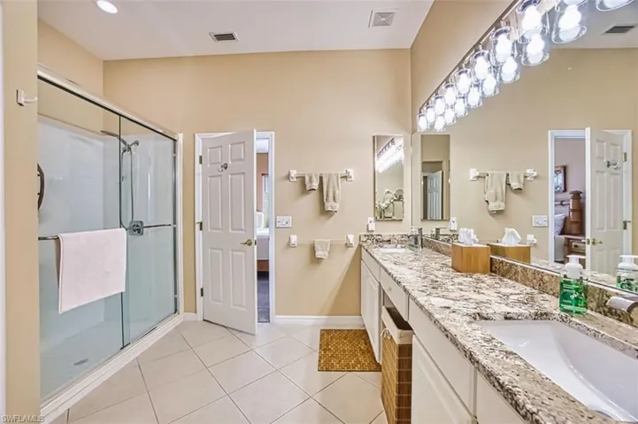 Ensuite bathroom with double vanity, a stall shower, and light tile patterned floors