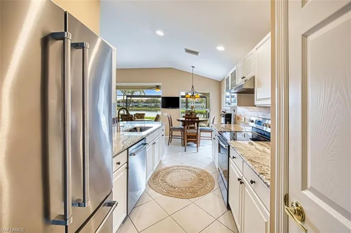 Kitchen with stainless steel appliances, vaulted ceiling, white cabinets, light stone counters, and suspended lighting