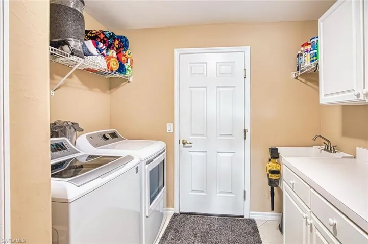 Laundry area featuring washing machine and dryer, cabinet space, and light tile patterned floors
