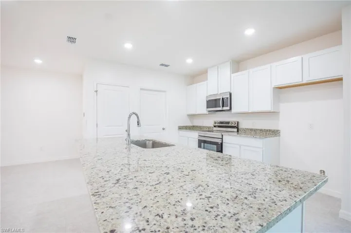Kitchen with stainless steel appliances, white cabinetry, an island with sink, recessed lighting, and light stone countertops