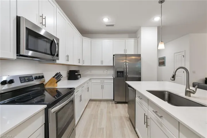 Kitchen featuring appliances with stainless steel finishes, pendant lighting, white cabinetry, light stone countertops, and light wood-style floors