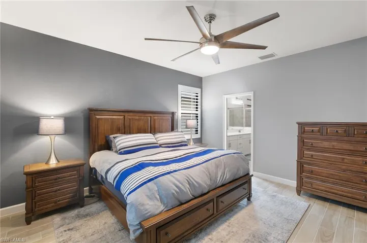 Bedroom with wood finish floors, a ceiling fan, and connected bathroom