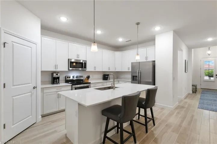 Kitchen featuring light wood-type flooring, a kitchen breakfast bar, decorative light fixtures, stainless steel appliances, and white cabinets