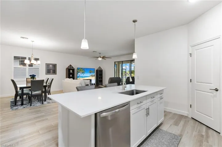 Kitchen with hanging light fixtures, dishwasher, white cabinets, and light wood-style flooring