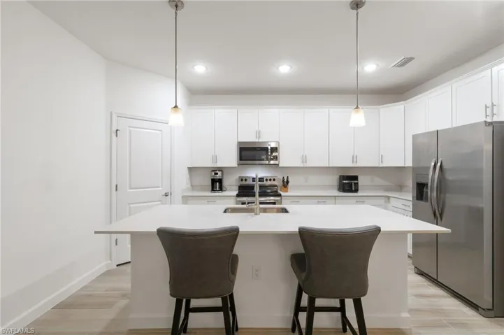 Kitchen with appliances with stainless steel finishes, an island with sink, white cabinets, a breakfast bar area, and pendant lighting