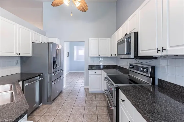 Kitchen with backsplash, appliances with stainless steel finishes, white cabinets, light tile patterned floors, and a high ceiling