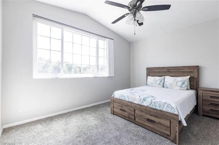 Carpeted bedroom featuring vaulted ceiling and a ceiling fan
