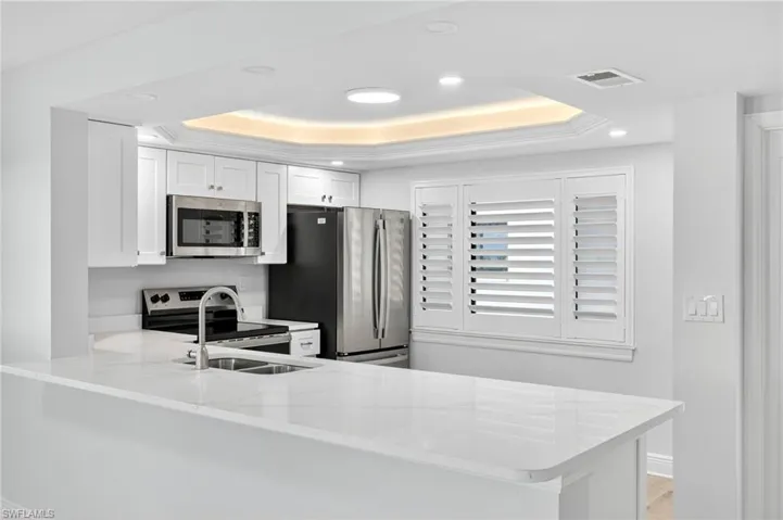 Kitchen with a peninsula, recessed lighting, white cabinetry, stainless steel appliances, and light quartz countertops