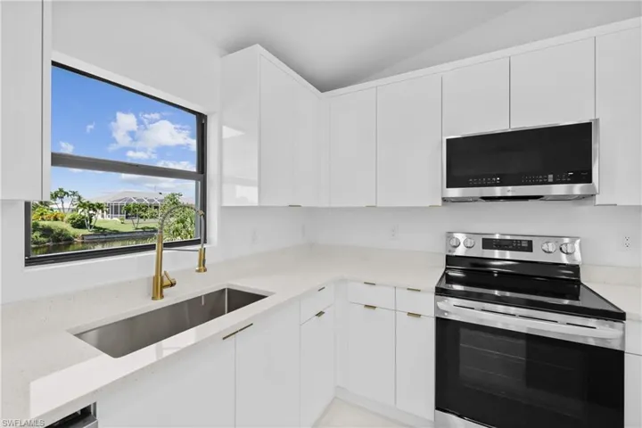 Kitchen with stainless steel appliances, lofted ceiling, white cabinets, and light stone counters