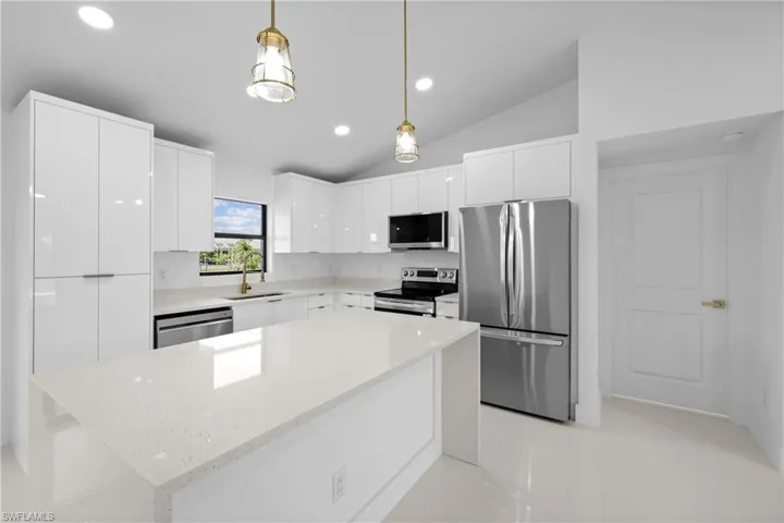Kitchen with modern cabinets, stainless steel appliances, white cabinets, vaulted ceiling, and pendant lighting