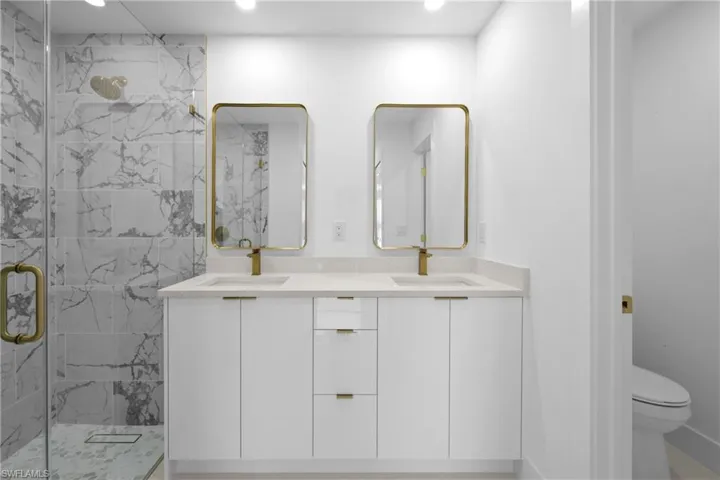 Bathroom featuring a marble finish shower, double vanity, and recessed lighting