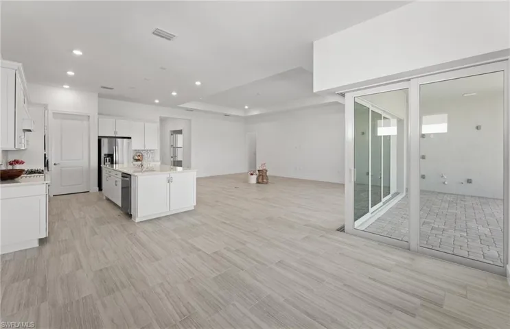 Kitchen featuring light tile flooring, a tray ceiling, an island with sink, white cabinets, and appliances with stainless steel finishes