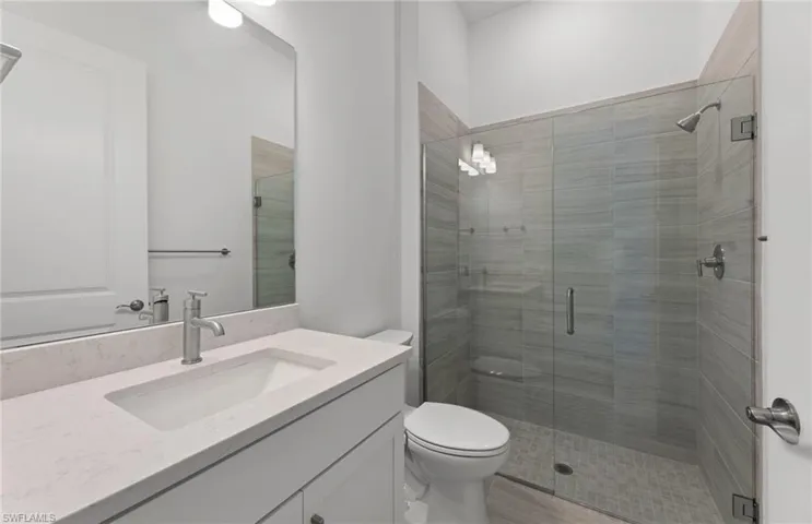 Bathroom featuring vanity with extensive cabinet space, toilet, and a shower with door