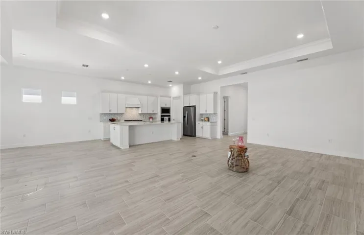 Unfurnished living room featuring ornamental molding, a tray ceiling, and light tile flooring