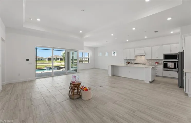 Kitchen with a center island with sink, custom range hood, stainless steel appliances, backsplash, and a raised ceiling