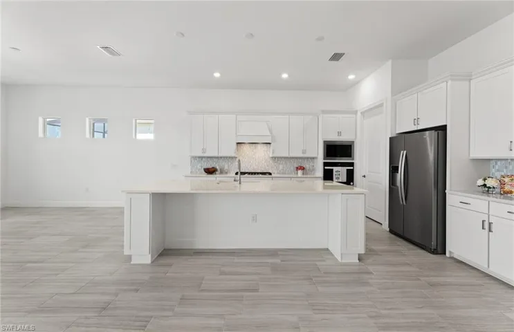 Kitchen with white cabinetry, custom range hood, a center island with sink, stainless steel appliances, and tasteful backsplash