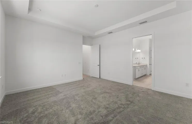 Unfurnished bedroom featuring a raised ceiling, connected bathroom, and carpet flooring