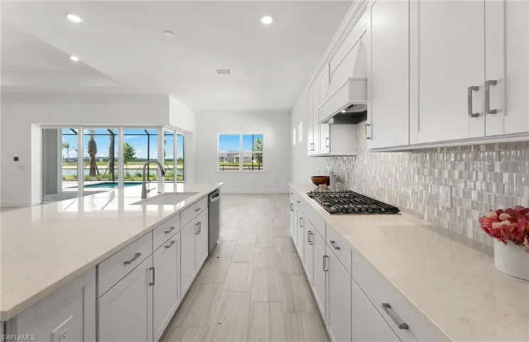 Kitchen with appliances with stainless steel finishes, white cabinets, light stone counters, backsplash, and sink