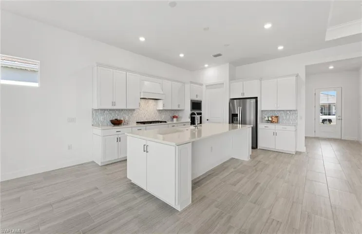 Kitchen featuring an island with sink, premium range hood, white cabinets, and tasteful backsplash