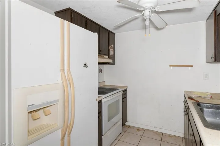 Kitchen with ceiling fan, dark brown cabinetry, white appliances, sink, and light tile patterned floors