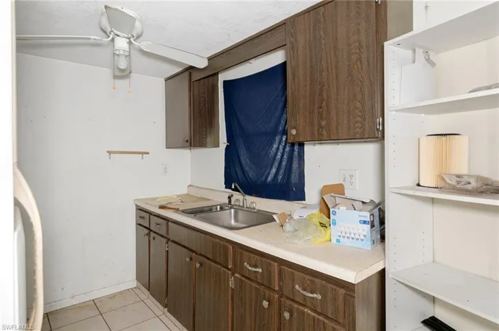 Kitchen with light tile patterned flooring, ceiling fan, sink, and dark brown cabinets
