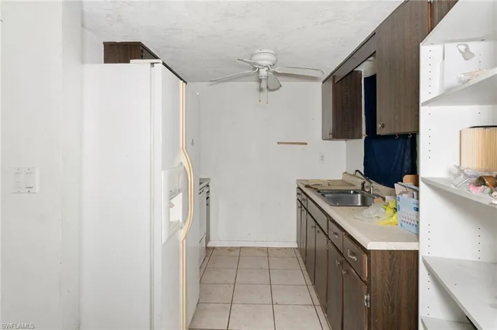 Kitchen featuring dark brown cabinetry, white fridge with ice dispenser, sink, and light tile patterned floors