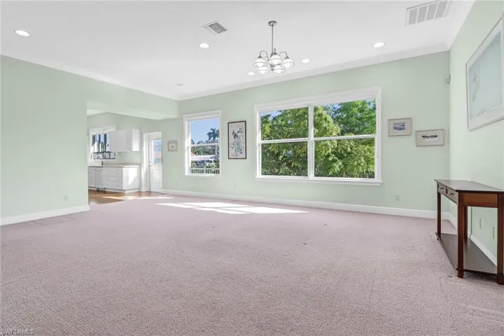 Unfurnished living room featuring crown molding, light colored carpet, and a chandelier