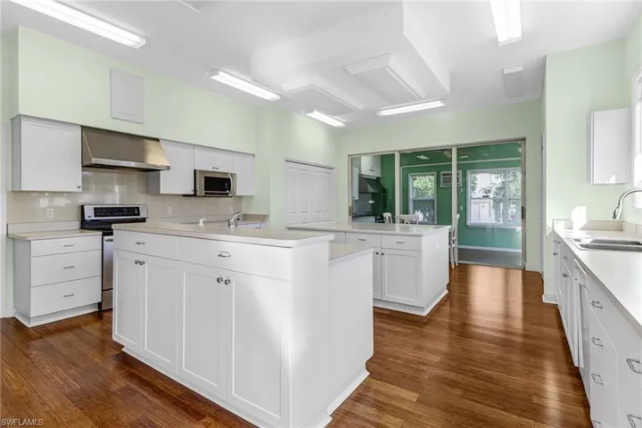 Kitchen with dark hardwood / wood-style floors, stainless steel appliances, wall chimney exhaust hood, and a center island with sink