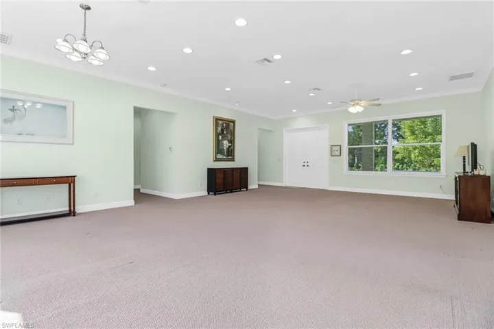 Unfurnished living room featuring carpet, ornamental molding, and ceiling fan with notable chandelier
