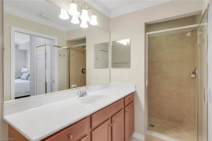 Bathroom with ornamental molding, an inviting chandelier, vanity, and a shower with shower door