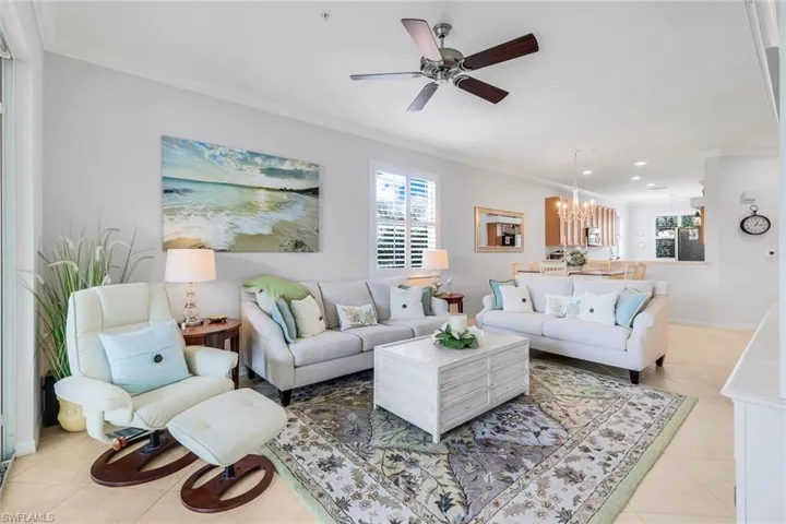 Tiled living room with ceiling fan with notable chandelier and ornamental molding
