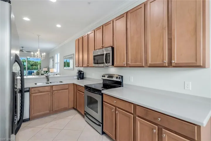 Kitchen featuring light tile patterned flooring, sink, an inviting chandelier, appliances with stainless steel finishes, and crown molding