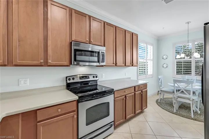 Kitchen featuring appliances with stainless steel finishes, pendant lighting, light tile patterned flooring, and ornamental molding