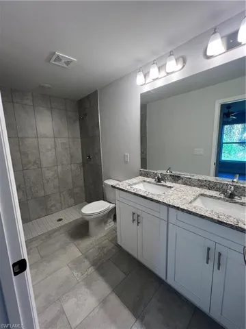 Bathroom with a tile shower, vanity, toilet, and ceiling fan