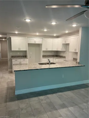 Kitchen featuring kitchen peninsula, light stone counters, ceiling fan, sink, and white cabinetry