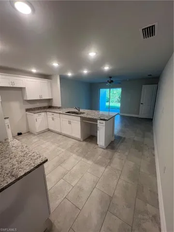 Kitchen with white cabinets, sink, ceiling fan, light stone countertops, and kitchen peninsula