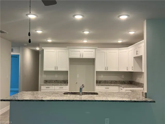 Kitchen featuring stone counters, kitchen peninsula, white cabinetry, and sink