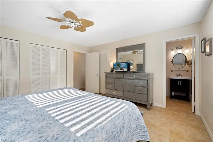 Bedroom with two closets, a ceiling fan, a textured ceiling, light tile patterned floors, and ensuite bathroom