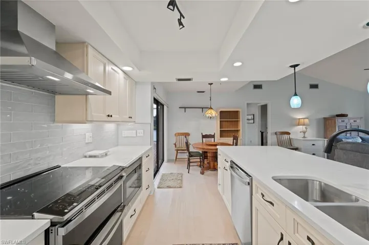 Kitchen featuring a raised ceiling, sink, hanging light fixtures, stainless steel appliances, and wall chimney exhaust hood
