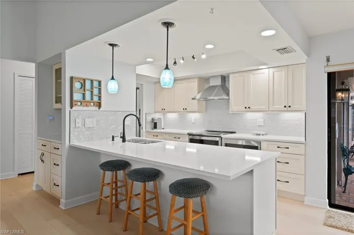 Kitchen with sink, white cabinetry, stainless steel range with electric cooktop, kitchen peninsula, and wall chimney exhaust hood