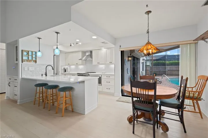Kitchen with wall chimney exhaust hood, sink, decorative light fixtures, kitchen peninsula, and white cabinets