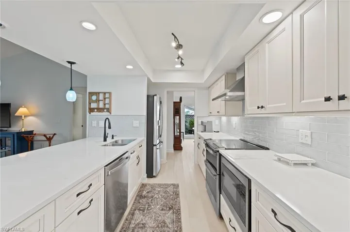Kitchen featuring pendant lighting, sink, wall chimney range hood, stainless steel appliances, and white cabinets