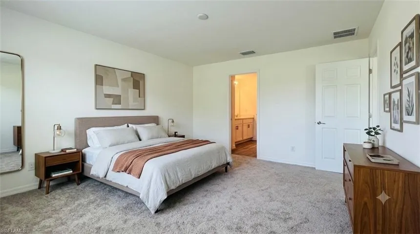 Spacious bedroom featuring plush carpeting, a multi-panel interior door, and an entryway to a full bathroom with a vanity