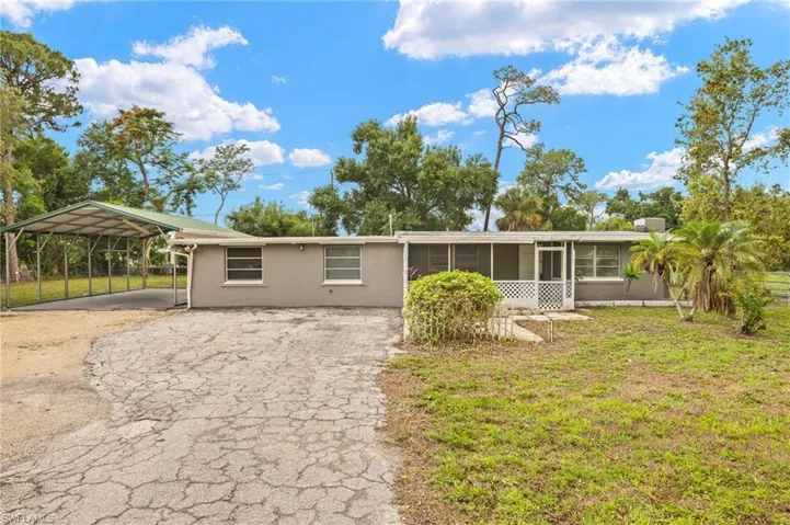 Ranch-style house with stucco siding, driveway, a sunroom, a detached carport, and a front yard
