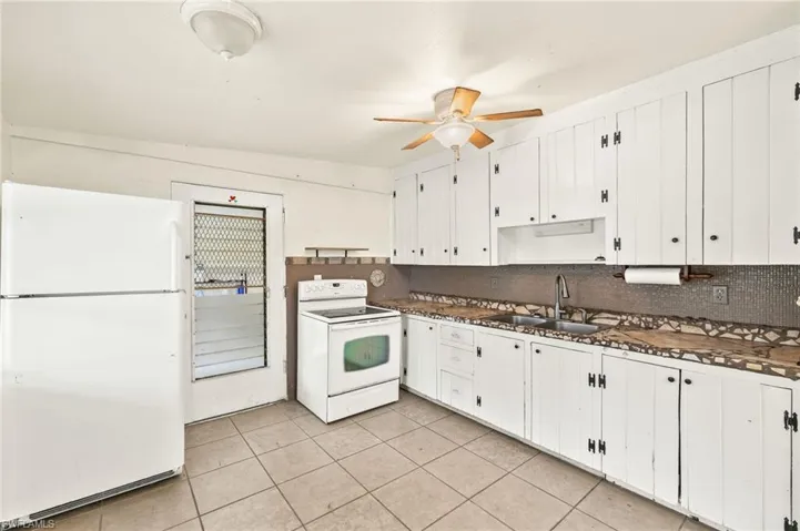 Kitchen with white appliances, dark countertops, a sink, ceiling fan, and light tile patterned floors