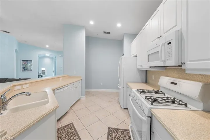 Kitchen with light tile patterned floors, white appliances, white cabinetry, sink, and decorative backsplash